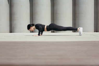 Spor eğitmeni sabah şınav çekiyor. Sokakta, parkta beton boruların arka planında geziniyor..