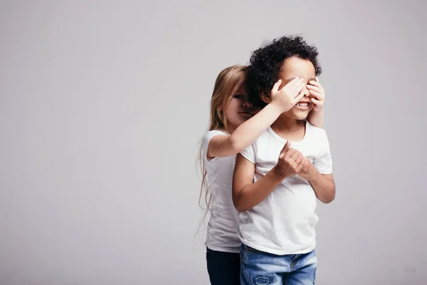 Het kleine meisje bedekte haar handen met de ogen van een zwarte jongen zodat hij kon raden wie er achter hem stond.. — Stockfoto