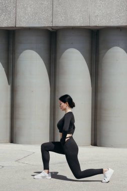 Spor üniformalı bir spor eğitmeni dizine oturdu ve parkta bacak kaslarını esnetti..