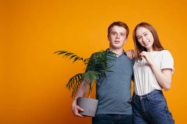 Девушка и парень стоят на фоне оранжевой стены. Молодой человек держит в руках чехол. — стоковое фото