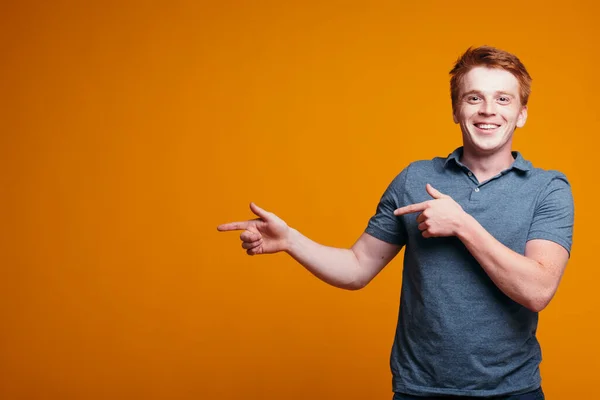 Рыжеволосый парень с пальцами появляется на пустом месте, чтобы вставить текст на оранжевом фоне. Рекламный баннер . — стоковое фото