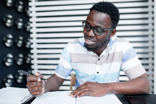 Ένας Αφρο-Αμερικανός φοιτητής με γυαλιά γράφει υλικό διαλέξεων στη βιβλιοθήκη για να προετοιμαστεί για μια εξέταση μετάφρασης στο πανεπιστήμιο. — Φωτογραφία Αρχείου