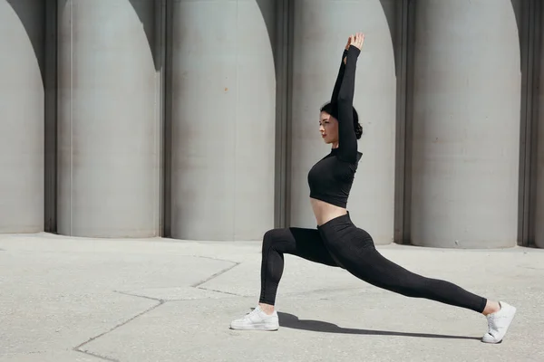 Profiel van Aziatische pilates trainer in zwart sportschoeisel gaat in voor sport op straat in het park lunchen naar voren en armen uitgestrekt. — Stockfoto