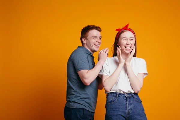 Рыжий парень и девушка смеются во время съемок в студии на оранжевом фоне . — стоковое фото