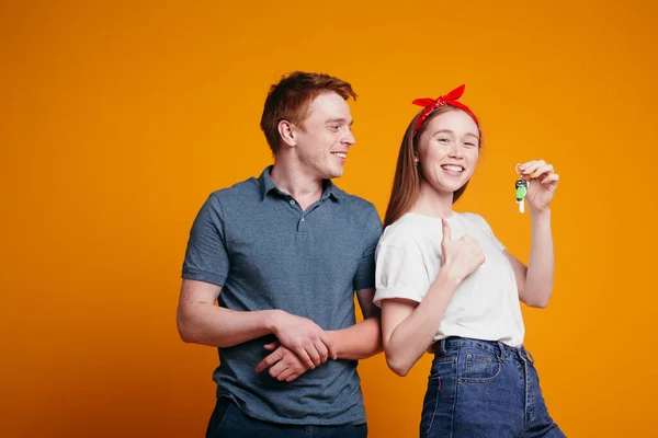Рыжеволосый парень и девушка радуются покупке новой квартиры и показывают большой палец вверх в знак успеха на оранжевом фоне в студии — стоковое фото