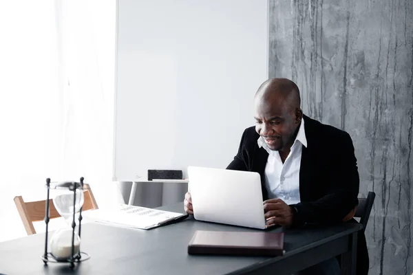 Темнокожий парень в деловом костюме, работающий за ноутбуком в офисе. Работник афроамериканец в крупной юридической фирме . — стоковое фото