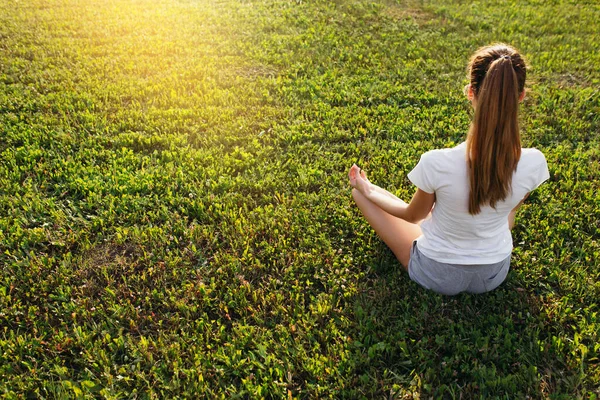 Bovenaanzicht vanaf de achterkant van een meditator in lotuspositie zittend op een groen gazon in de natuur bij dageraad. — Stockfoto
