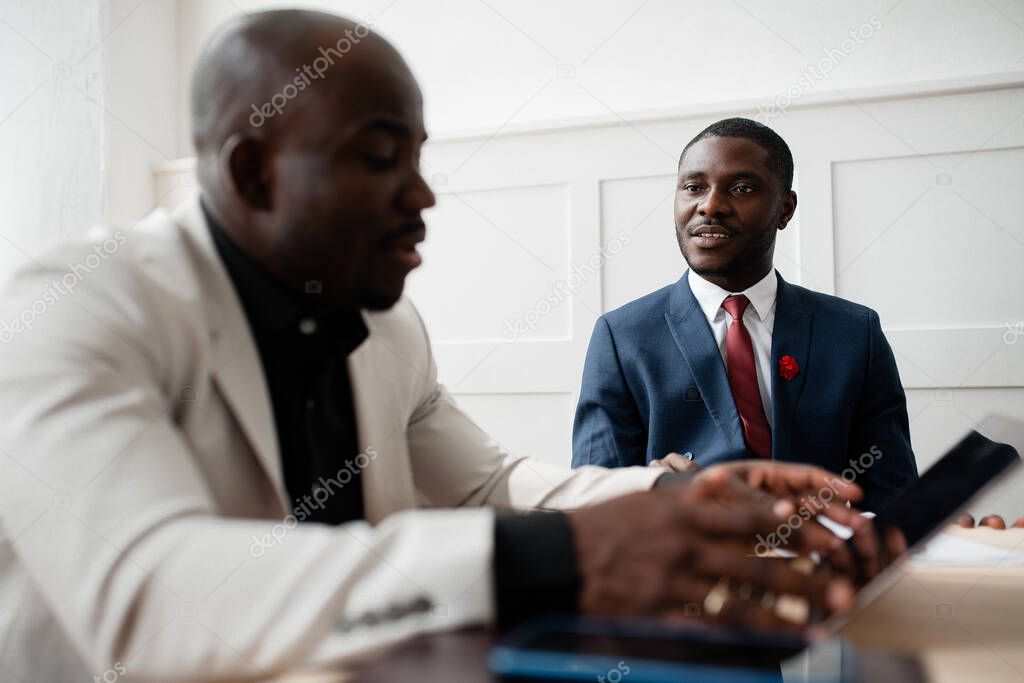 Two dark-skinned investors in suits are sitting nearby and discussing investment options for their money sitting in the companys office.