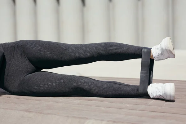 Foto close-up dari gadis olahraga kaki dengan karet olahraga gelang di pergelangan kaki. Latihan berbaring di sisi Anda mengangkat satu kaki. — Stok Foto