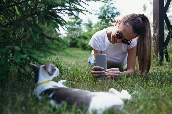 A young girl photographs lying on the ground her oriental cat resting on the grass in nature.