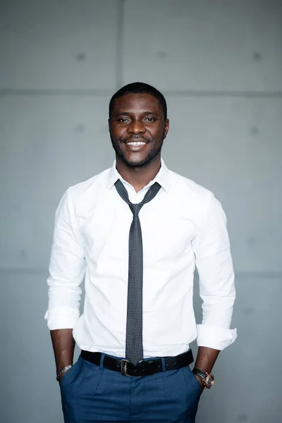 Retrato de um homem negro com uma camisa branca de pé com as mãos nos bolsos e sorrindo para a câmera . — Fotografia de Stock