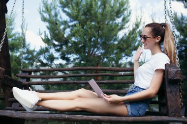 Bir kız, sokak salıncağında oturur ve arkadaşlarıyla dizüstü bilgisayarla iletişim kurar. Doğadaki kendini izole etme ile ilgili iletişim