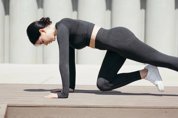 노천 공원에서 두 팔 다리로 서서 가슴까지 무릎을 굽히고 운동을 하고 있는 아시아 여자의 모습 — 스톡 사진
