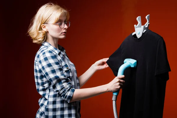 Κορίτσι χειμώνας εργαζόμενος καθαρισμό ένα σκούρο γυμνό πουκάμισο σε μια κρεμάστρα. η ταχεία αφαίρεση πτυχώσεων στα ενδύματα με ατμό. — Φωτογραφία Αρχείου