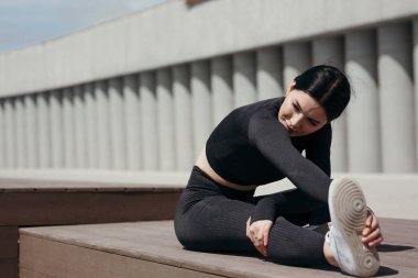 Kız sporcu, tahta bir bankta esnemiş bir bacağa eğiliyor. Dışarıdaki Yoga Egzersizleri