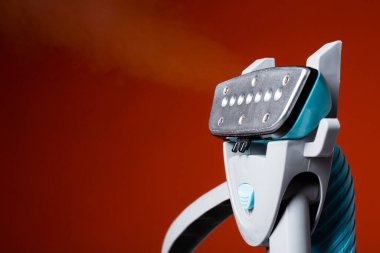 Buharlı hortumun yakın çekimi kırmızı arka plandaki kıyafetleri ütülemek için ıslak buhar yayıyor..