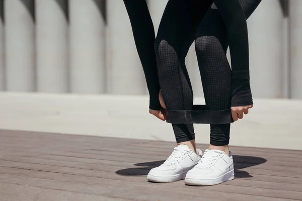 一名运动员的女运动员的脚的近照，她用一条运动橡皮筋把一个女运动员的脚绑在自己的脚上，这个女运动员在公园的大街上做运动 — 图库照片
