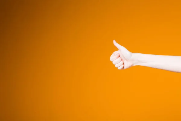 Kobieta na pomarańczowym tle pokazuje kciuki w górę w porozumieniu i akceptacji. Ręka do użycia na banery i witryny. — Zdjęcie stockowe