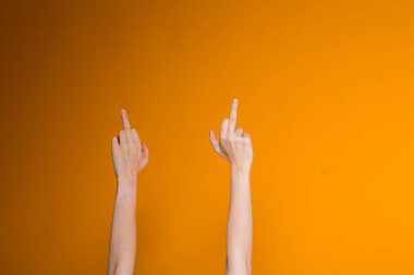 Kadın elleri kameraya orta parmaklarını gösteriyor. Turuncu arka planda agresif kışkırtıcı hareketler..