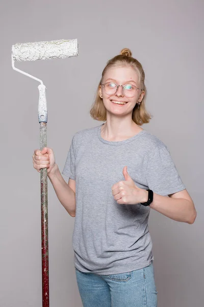 Señora divertida pintor profesional de la casa sonriendo y mostrando el pulgar. Trabajador atractivo con un rodillo de construcción . —  Fotos de Stock