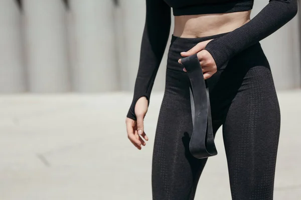 Primer plano del cuerpo en forma de una mujer sosteniendo en sus manos una goma deportiva negra para entrenar al aire libre en el parque —  Fotos de Stock