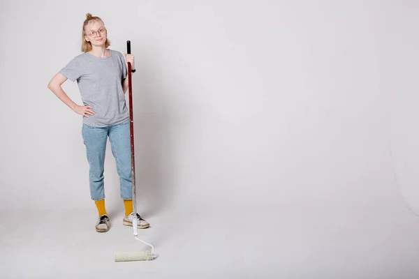 Atractiva chica rubia de pie sobre fondo blanco y sosteniendo un rodillo profesional de la construcción para la reparación . —  Fotos de Stock