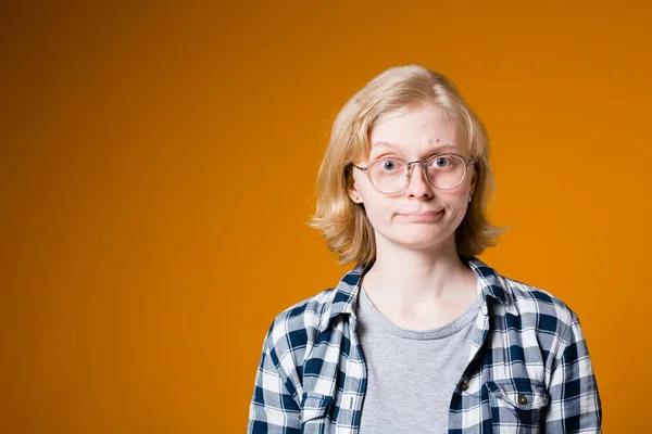 Ξανθιά κοπέλα με καρό πουκάμισο με γυαλιά και σκληρή ματιά στην κάμερα σε πορτοκαλί φόντο. — Φωτογραφία Αρχείου