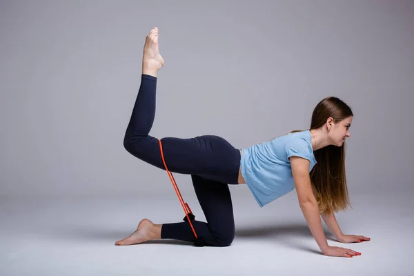 Girl yoga trainer in profile shows exercises on the legs with the help of an elastic expander on the hips on a white background — Stock Photo, Image