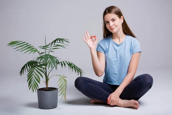 Портрет дівчини, що сидить у положенні лотоса поруч із зеленою квіткою і показує її знак з пальцями на білому ізольованому фоні — стокове фото
