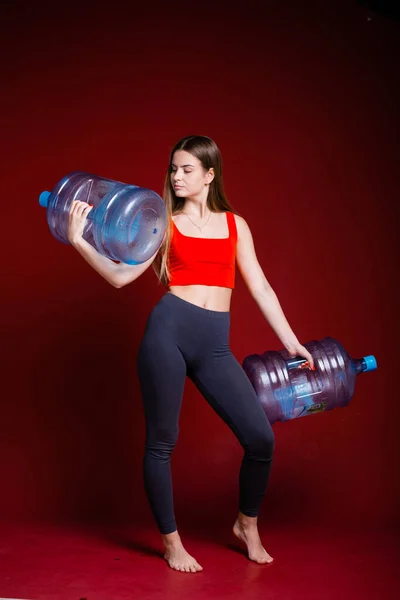 Портрет повнометражної дівчини, яка тримає дві кулі очищеної води для доставки додому на червоному тлі — стокове фото