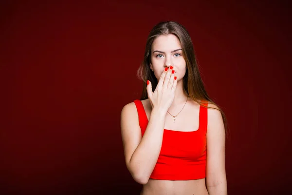 Chica italiana mirando a la cámara y cubriéndose la boca con la mano como señal de silencio y guardando secretos sobre un fondo borgoña —  Fotos de Stock