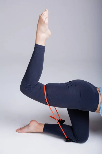 Meisje yoga trainer in profiel toont oefeningen op de benen met behulp van een elastische expander op de heupen op een witte achtergrond — Stockfoto