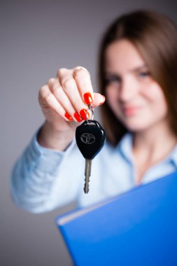Gri arkaplanda yeni bir arabanın anahtarlarını ve veri klasörünü elinde tutan bir araba satıcısı kızın portresi