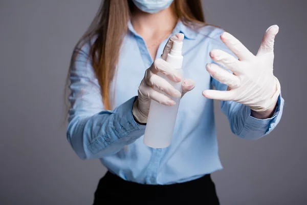 Κοντινό πλάνο ενός κοριτσιού που εργάζεται σε γραφείο με ιατρική μάσκα και πασπαλίζει αντισηπτικό στα γάντια προκειμένου να προληφθεί η ασθένεια από ασθένειες σε γκρι φόντο — Φωτογραφία Αρχείου