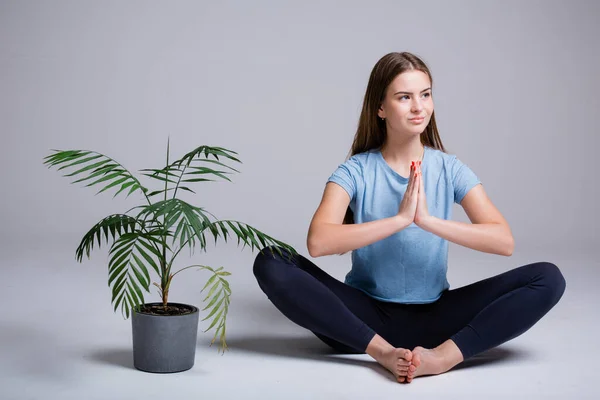 Portrait of yoga trainer girl sitting in lotus position on a white background next to a green flower — Stock Photo, Image