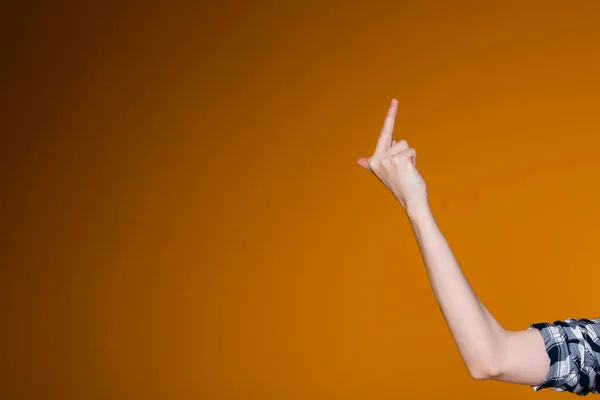 A mão feminina mostra o dedo médio à direita da tela em um fundo laranja. O conceito de gestos indecentes e desafiadores — Fotografia de Stock