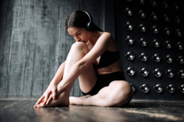 Siyah spor elbiseli bir kız. Ellerinin kaslarını esnetmesi ve kulaklıkla müzik dinlemesi için yoga egzersizleri yapıyor..