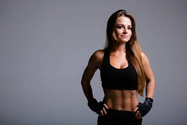Girl athlete with a relief straight abdominal muscles posing in black top and pants on a gray background. — Stock Photo, Image