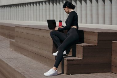 Sabah yürüyüşü sırasında dizüstü bilgisayarı olan bayan sporcu işten önce dinleniyor. Kumral kucağında bilgisayarla oturuyor..