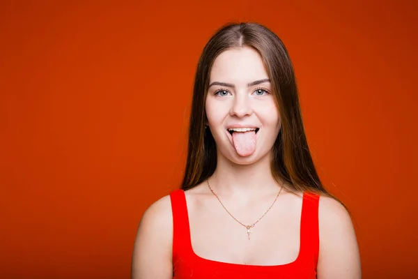 Roztomilé zlobivé dívka evropského vzhledu ukazuje svůj jazyk do kamery na oranžovém pozadí — Stock fotografie