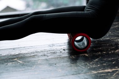 Close-up of hip and butt of a girl in black leggings. Exercising a massage roll of the fascia of the posterior muscles of the thighs and buttocks in the gym