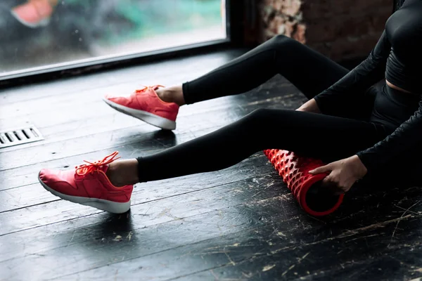 Close-up de pernas em leggings pretos de uma menina que colocou um rolo de massagem sob seus músculos traseiros para trabalhar através da fáscia . — Fotografia de Stock