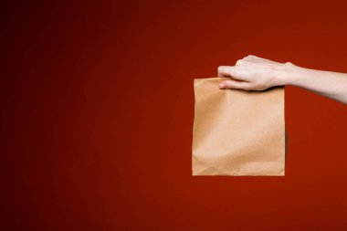 Uzamış kadın eli kırmızı arka planda bir kese kağıdı tutuyor. Yemek ve hediye teslimatı..