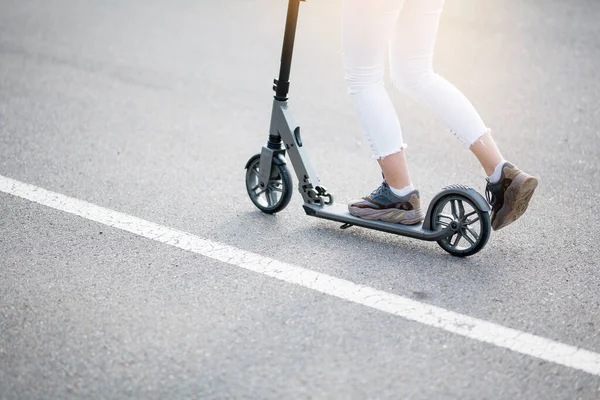 Primer plano de la parte inferior de un scooter y las piernas de una chica que está montando por la calle en los vehículos adquiridos —  Fotos de Stock