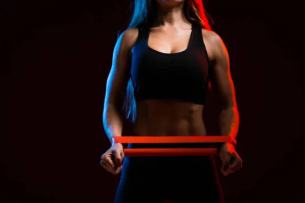 Close-up com iluminação de néon, o corpo de uma menina-atleta, e com uma prensa inflada e mãos fazendo exercícios com um expansor elástico nas mãos . — Fotografia de Stock