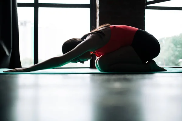 Profilul unei fete care face yoga pe covor. Poza unui copil sau a unui balaban vizavi de o fereastră panoramică . — Fotografie, imagine de stoc