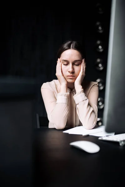 Trabajadora de oficina sentada en una camisa clásica y cansada frota su whisky con los ojos cerrados mientras está sentada en una mesa en la oficina . — Foto de Stock