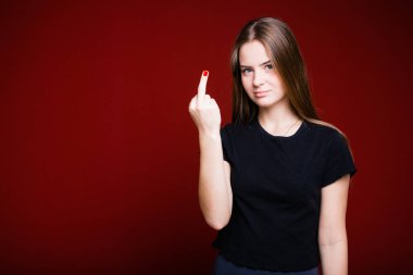 The concept of uncivilized gestures. A girl with long hair and in a black T-shirt shows the middle finger on a red background. clipart