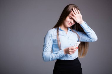 Ofis çalışanı kendini iyi hissetmiyor ve gri arka planda soğuk algınlığı ilacı alırken elini alnının yakınında tutuyor.