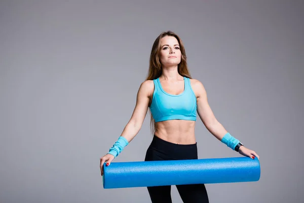 Un entrenador de Pilates en un top deportivo azul y una prensa inflada sostiene un cilindro de paralón largo para trabajar la fascia de los músculos del cuerpo en el estudio . —  Fotos de Stock